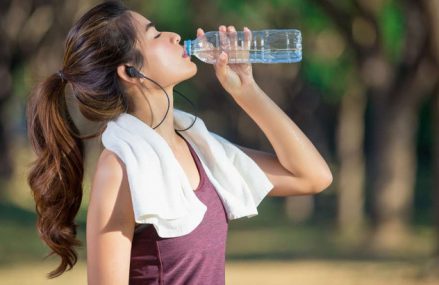 Девушка в наушниках с полотенцем на шее пьет воду из бутылки