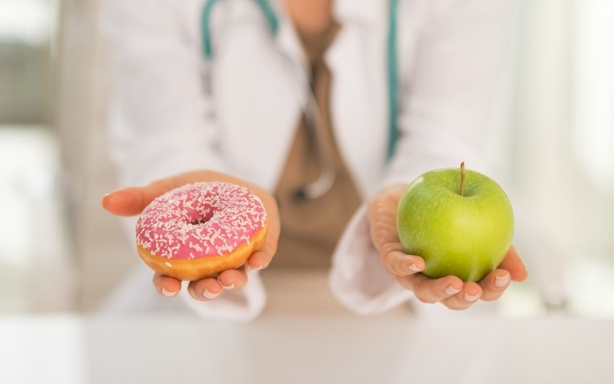 Лікар в одній руці тримає пончик, а в другій яблуко