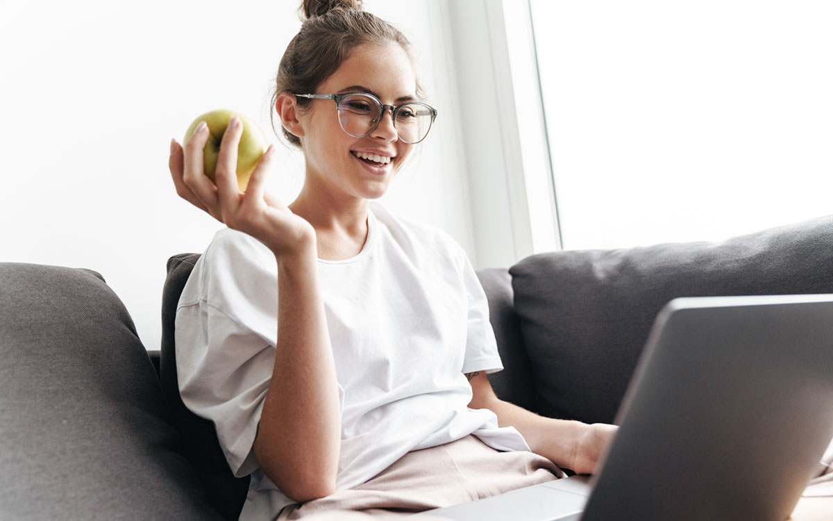 Дівчина на дивані з яблуком і ноутбуком
